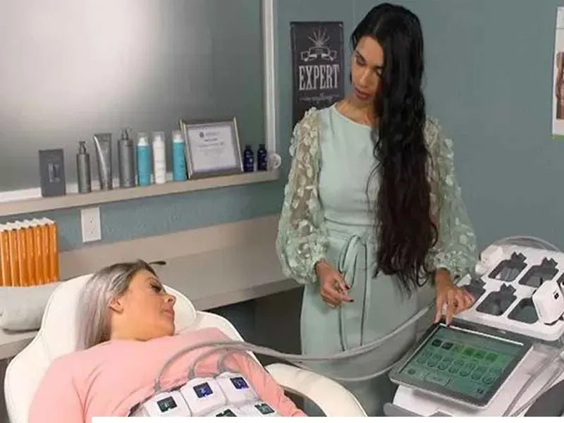 یه خانم روی تخت دراز کشیده و الکترودای دستگاه ترواسکالپ بهش وصله و یه خانم جوان که اپراتور هست بالا سرش ایستاده و داره با مانیتور دستگاه ی لاغری رو تنظیم میکنه برای لاغری شکم و پهلو بیمار